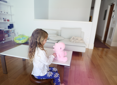 Child playing with a pink teddy bear on a table in a living room.