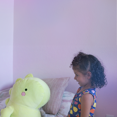 Child with a large green dinosaur toy in a room with a pink wall.